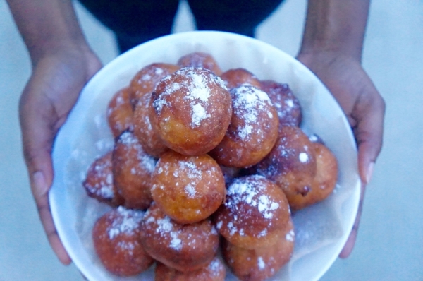 Nigerian puff puff balls in a bowl being held by hand with icing sugar on it