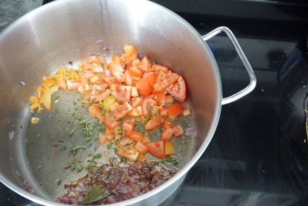 A pot with oil thyme bay leaf chopped tomato onions and pepper