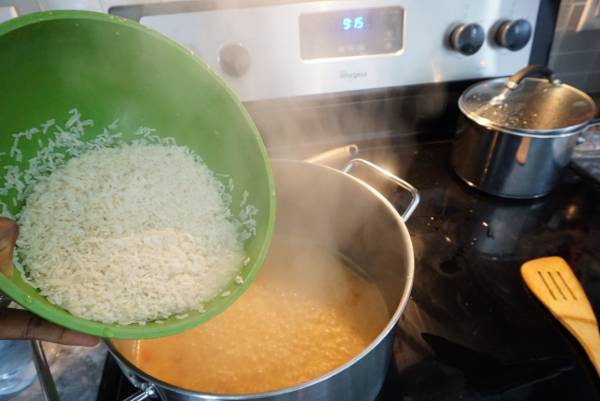 Washed parboiled rice in a green bowl being added to boiling coconut milk 