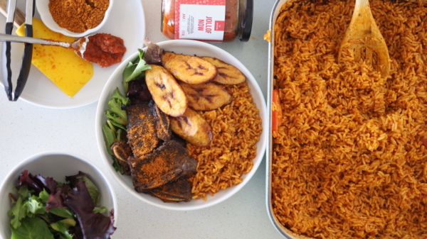 Jollof rice in a white bowl with vegetables fried plantain and beef suya