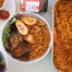 Jollof rice in a white bowl with vegetables fried plantain and beef suya