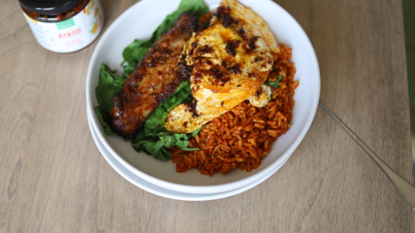 Plate of jollof rice with fried egg atasu pepper sauce grilled turkey wing and spinach 